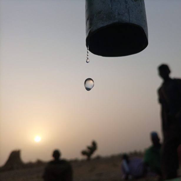 Das Bild symbolisiert den Klimawandel in Nigeria, der zu Dürren führt. Zu sehen ist ein Wassertropfen, der aus einem Rohr rint; im Hintergrund, Menschen, die in der Nähe sind.
